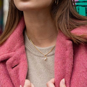Detail of S925 sterling silver heart topaz necklace worn over a stylish pink wool coat