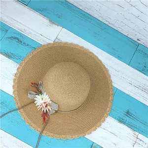 Detailansicht Strohhut in Khaki mit Blumenverzierung und Wellenrand auf Holz