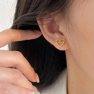 Macro shot of minimalist gold heart stud earrings crafted with tiny metal spheres on ear