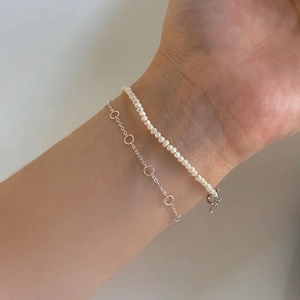 Detail of layered S925 sterling silver chain and delicate white pearl bracelet for women