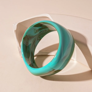 Macro shot of wide acrylic bangle with teal and brown marble pattern on white stand