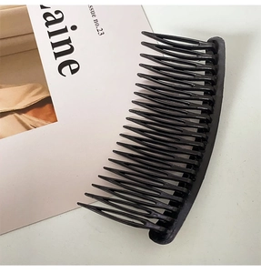 Detail view of a black plastic hair comb clip on a minimalist beige background