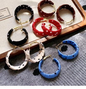 Macro detail of geometric polka dot fabric hoop earrings in five retro colors on a linen tray