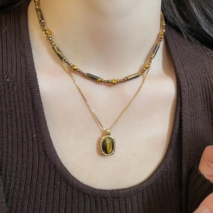 Detail of double-layer golden chain necklace with brown tiger eye stone on a brown sweater