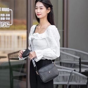 Close-up of black V-quilted crossbody bag with wide canvas strap and mini coin pouch