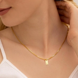 Close-up of golden rectangular letter G pendant on a delicate box chain necklace