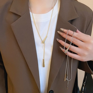 Detail view of minimalist gold and silver teardrop necklaces on a brown suit and white tee