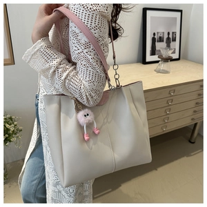 Dettaglio della borsa tote crema con spalline rosa e ciondolo su modella donna