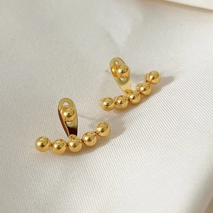 Elegant gold beaded arc stud earrings with polished metal spheres on fabric background