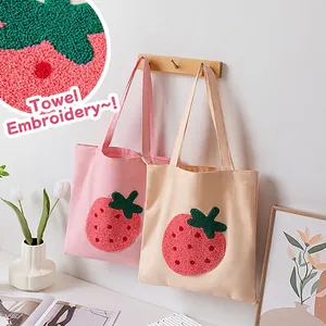 Pink and beige canvas tote bags with 3D strawberry embroidery hanging on a rack