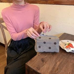 Corduroy cosmetic bag with large dots held by hand in a cozy cafe setting scene