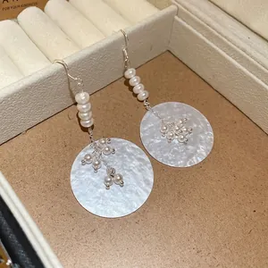 Elegant pearl drop earrings with round shell pendant on creamy jewelry display tray