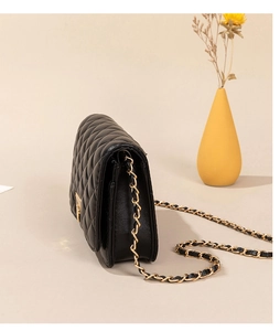 Side view of black quilted leather shoulder bag with golden metal chain and soft lighting