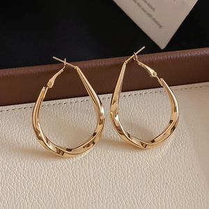 Detailed macro view of golden twisted teardrop earrings on white leather texture