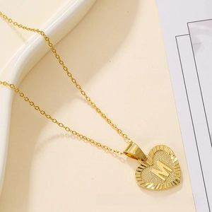 Detailed view of a gold heart pendant featuring an embossed M letter on a wave plate