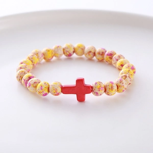Close-up of beaded bracelet with colorful spotted beads and a red cross charm