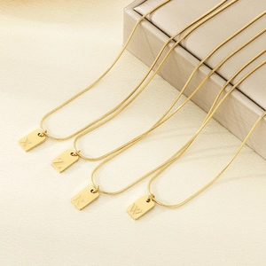 Detail van vierkante gouden hangers met initialen X Z R W aan roestvrijstalen ketting