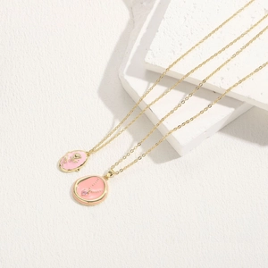 Close-up of pink enamel heart and rose pendants on gold chains on white stone display