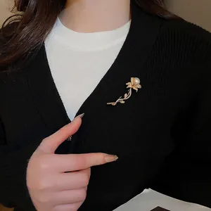 Elegant gold flower brooch with white pearl and crystals on black cardigan