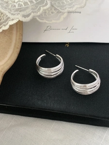 Detailed macro view of silver multi-layer C-shaped stud earrings on a black display box