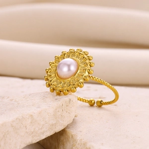 Macro detail of a gold rope ring with a central pearl and sunburst motif on stone