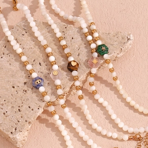 Detail view of white shell beads and hexagonal natural stone pendants on gold necklaces