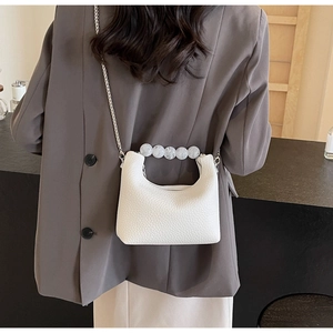 White textured leather handbag with pearl handle and silver chain worn with a grey blazer