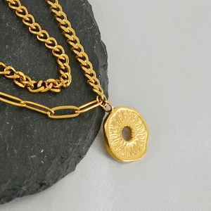 Double-layered golden stainless steel necklace with daisy pendant on textured stone