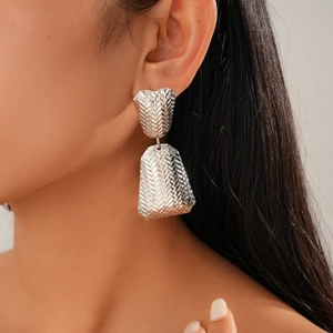 Detail shot of long silver geometric earrings with textured woven metal on model
