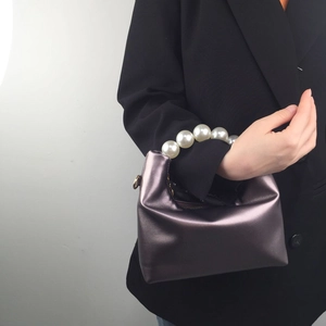 Detail of purple metallic pillow bag with pearl handle held by a model in a black suit