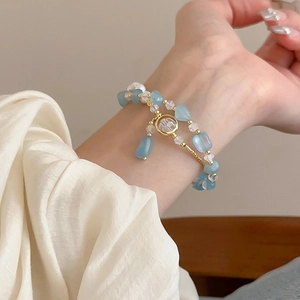 Dettaglio del bracciale con cristalli azzurri e perle con catena d'oro su seta