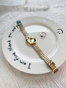 Flat lay of a gold square women's watch and matching ring on a white ceramic plate
