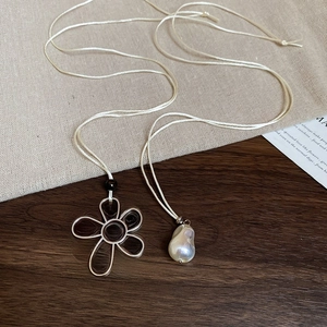 Detail of flower-shaped silver frame pendant with irregular baroque pearl on beige cord