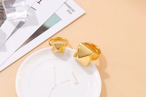 Close-up of geometric pyramid gold rings on a white ceramic plate with zodiac detail