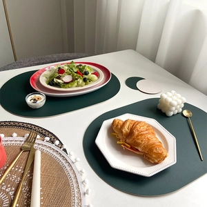 Oval dark green PU leather place mat and round coaster set on a modern white dining table