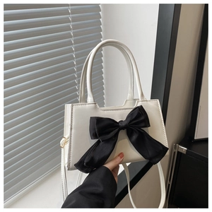 Detail of white leather handbag with a large black bow and sturdy top handle