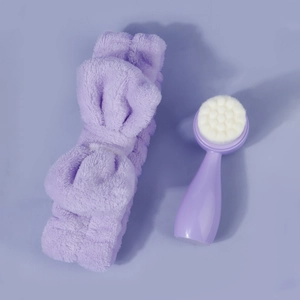 Macro shot of purple plush bow headband and dual-sided silicone face cleansing brush