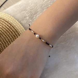 Handmade woven seed bead bracelet with a central white pearl on a model's wrist