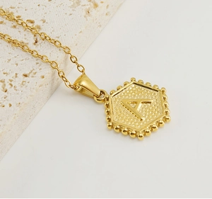 Close-up of golden hexagonal pendant with letter A engraving and beaded edge detail