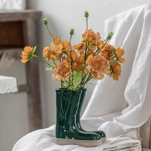 Creative dark green boot-shaped ceramic flower pots with orange flowers on wood shelf