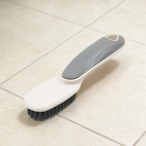 Détail de brosse à chaussures avec manche gris, trou de suspension et poils noirs denses