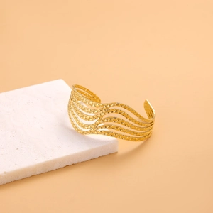 Detailed view of layered hollow wave pattern on gold open bangle over marble block