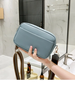 Detail of blue-grey pebble leather camera bag featuring a striped wide shoulder strap