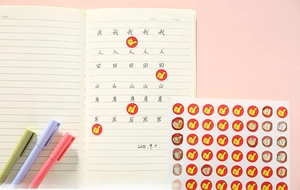 Close-up of red thumbs-up reward stickers on a notebook with colorful stationery pens