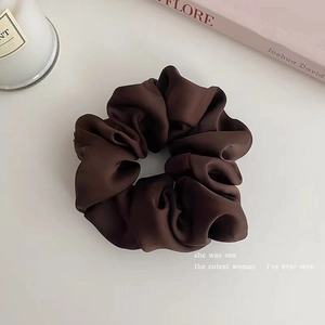 Detail of a dark brown satin scrunchie with silky pleats on a minimalist background