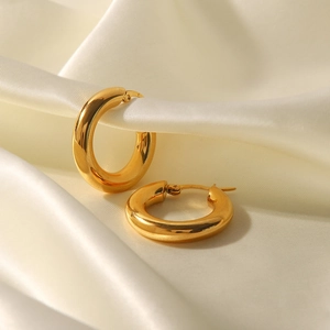 Polished gold chunky hoop earrings displayed on premium cream silk fabric background