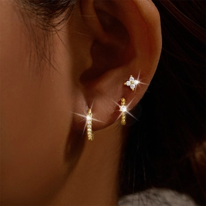 Close-up of gold s925 silver earring set with zircons and floral stud on model's ear
