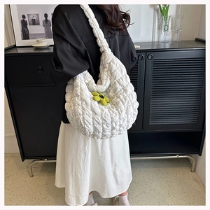 Close-up of a white quilted dumpling tote bag with a yellow flower charm accessory