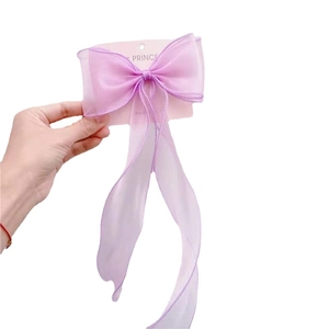 Hand holding a purple organza bow hair clip with long ribbons on a display card