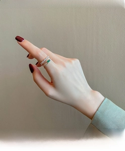 Stacked gold rings featuring emerald gemstone and small crystals on a model hand